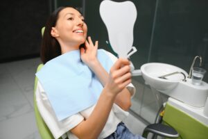 Young woman smiling and admiring her teeth in a mirror after dental check-up in Macquarie Fields clinic